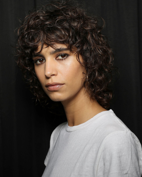 A model wearing a curly wolf cut and white tshirt